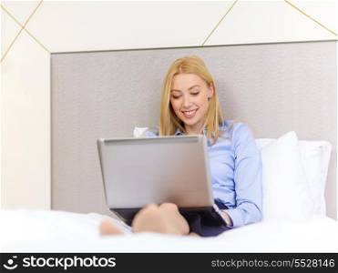 business, technology, internet and hotel concept - happy businesswoman with laptop computer lying in hotel in bed