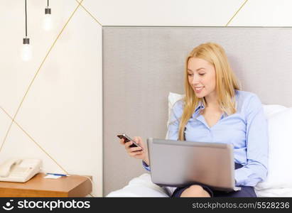 business, technology, internet and hotel concept - happy businesswoman with smartphone and laptop lying in hotel in bed