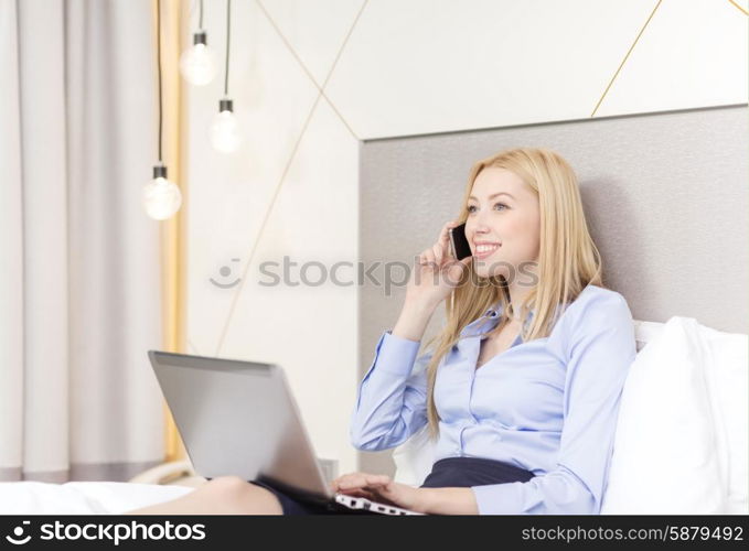 business, technology, internet and hotel concept - happy businesswoman with smartphone and laptop lying in hotel in bed