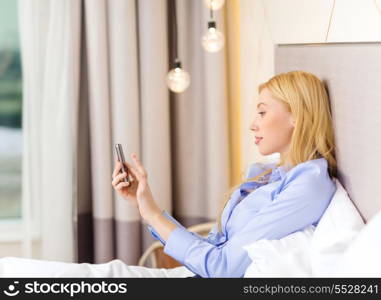 business, technology, internet and hotel concept - happy businesswoman with smartphone lying in hotel in bed