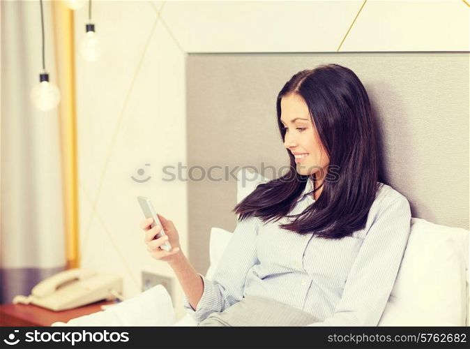 business, technology, internet and hotel concept - happy businesswoman with smartphone lying in hotel in bed