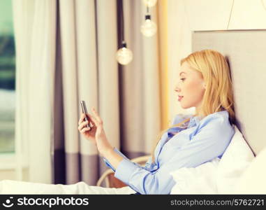 business, technology, internet and hotel concept - happy businesswoman with smartphone lying in hotel in bed