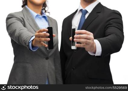 business, technology, internet and office concept - businessman and businesswoman with blank black smartphone screens in office