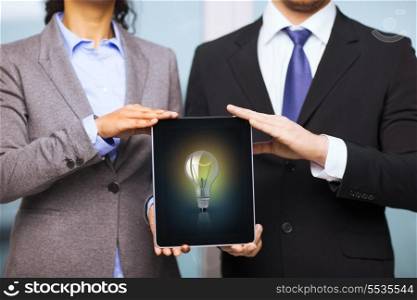 business, technology, internet and office concept - businessman and businesswoman with bulb on tablet pc screen in office