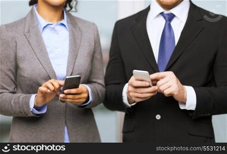 business, technology, internet and office concept - businessman and businesswoman with smartphones in office