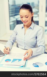 business, technology, internet and office concept - smiling businesswoman with laptop and charts in office