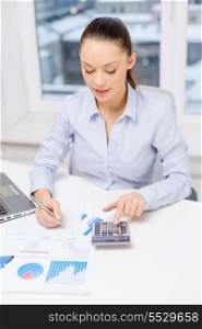 business, technology, internet and office concept - smiling businesswoman with laptop, calculator and charts in office