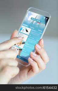 business, technology, internet and people concept - close up of woman hand holding and showing transparent smartphone with news web pages on screen