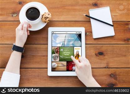 business, technology, mass media and people concept - close up of woman with news on tablet pc computer screen, notebook and coffee on wooden table