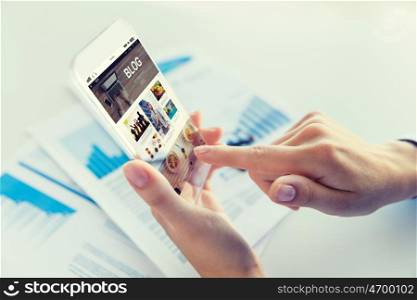 business, technology, media, internet and people concept - close up of woman hand holding and showing transparent smartphone with blog web page on screen at office