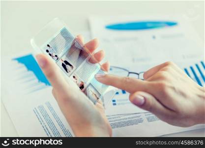 business, technology, news, mass media and people concept - close up of woman hand holding transparent smartphone with web page on screen at office