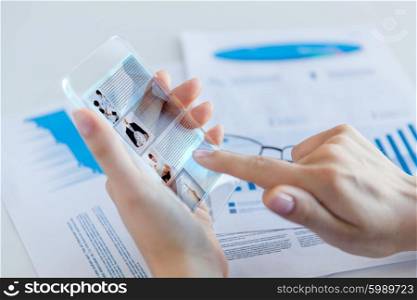 business, technology, news, mass media and people concept - close up of woman hand holding transparent smartphone with web page on screen at office