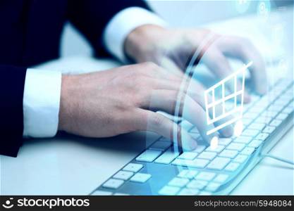 business, technology, online commerce and internet concept - close up of businessman hands typing on keyboard with shopping trolley hologram
