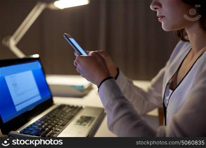 business, technology, overwork, deadline and people concept - close up of businesswoman with smartphone at night office. businesswoman with smartphone at night office