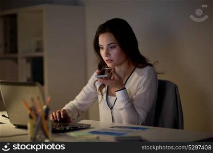 business, technology, overwork, deadline and people concept - woman with laptop and smartphone using voice command recorder at night office. woman using voice command recorder on smartphone