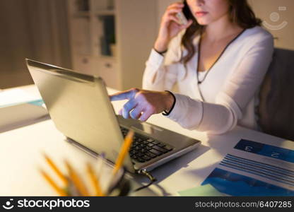 business, technology, overwork, deadline and people concept - woman with laptop calling on smartphone at night office. woman with laptop calling on smartphone at office