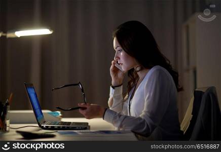 business, technology, overwork, deadline and people concept - woman with laptop calling on smartphone at night office. woman with laptop calling on smartphone at office. woman with laptop calling on smartphone at office
