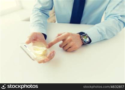 business, technology, startup and people concept - close up of male hand holding and showing transparent smart phone and watch at office with light bulb symbol on screen