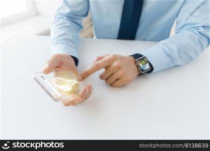 business, technology, startup and people concept - close up of male hand holding and showing transparent smart phone and watch at office with light bulb symbol on screen