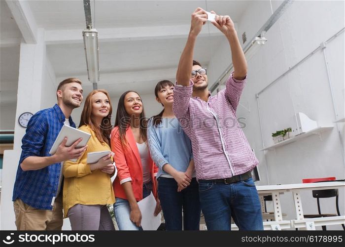 business, technology, startup and people concept - happy international creative business team taking selfie at office