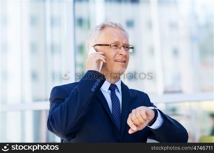 business, technology, time, punctuality and people concept - senior businessman calling on smartphone with wristwatch or smart watch on his hand in city