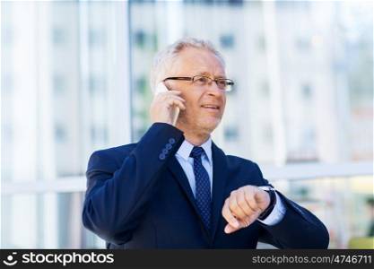 business, technology, time, punctuality and people concept - senior businessman calling on smartphone with wristwatch or smart watch on his hand in city