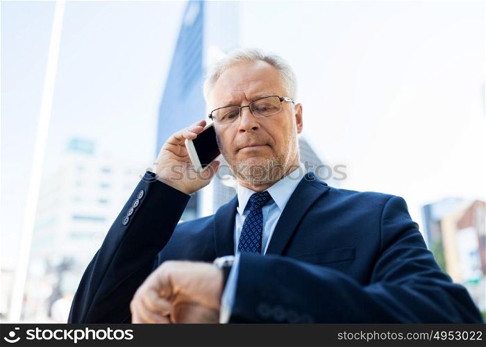 business, technology, time, punctuality and people concept - senior businessman calling on smartphone an looking at wristwatch or smart watch on his hand in city. senior businessman calling on smartphone in city