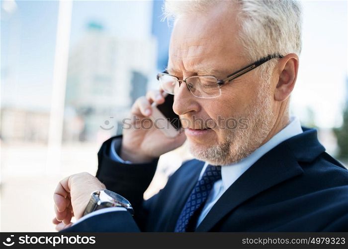 business, technology, time, punctuality and people concept - senior businessman calling on smartphone an looking at wristwatch in city. senior businessman calling on smartphone in city