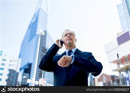business, technology, time, punctuality and people concept - senior businessman calling on smartphone with wristwatch or smart watch on his hand in city. senior businessman calling on smartphone in city