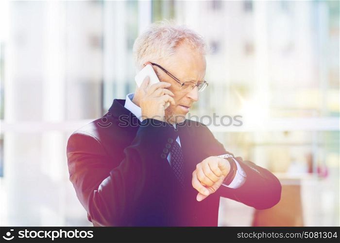 business, technology, time, punctuality and people concept - senior businessman calling on smartphone an looking at wristwatch in city. senior businessman calling on smartphone in city