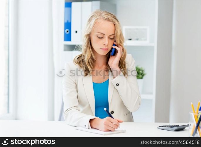 business, tecnology, communication and people concept - businesswoman with pen and notebook calling on smartphone at office