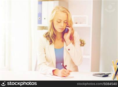 business, tecnology, communication and people concept - businesswoman with pen and notebook calling on smartphone at office. businesswoman calling on smartphone at office. businesswoman calling on smartphone at office