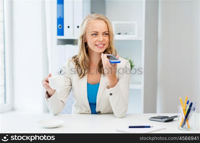 business, tecnology, communication and people concept - happy businesswoman drinking coffee and using voice command or recorder on smartphone at office