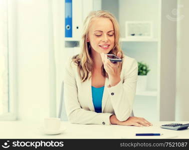 business, tecnology, communication and people concept - happy businesswoman drinking coffee and using voice command or recorder on smartphone at office. businesswoman using voice command on smartphone