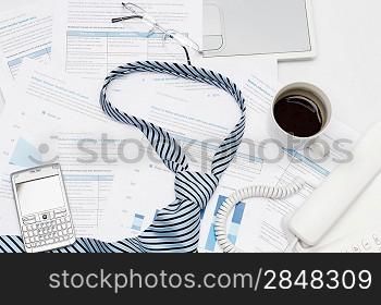 Business tie on busy office desk paper charts, phone coffee
