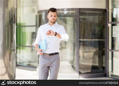 business, time and people concept - young man with folder looking at wristwatch on city street
