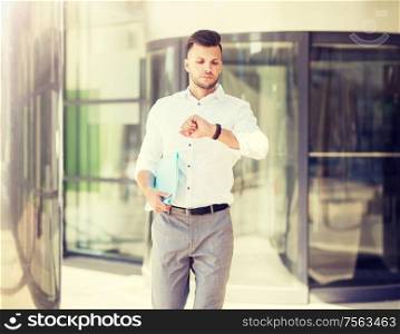 business, time and people concept - young man with folder looking at wristwatch on city street. man with folder looking at wristwatch on street