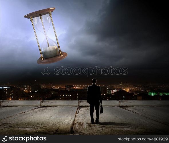 Business time. Conceptual image with sandglass and rear view of businessman