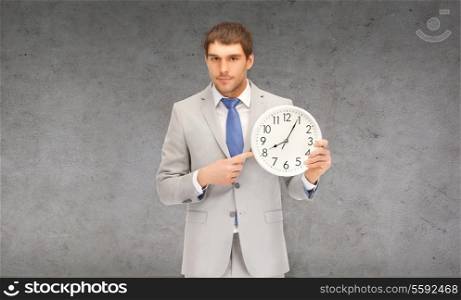 business, time magement and office concept - handsome businessman pointing finger to wall clock