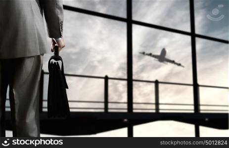 Business travel. Back view of businessman at airport with suitcase in hand