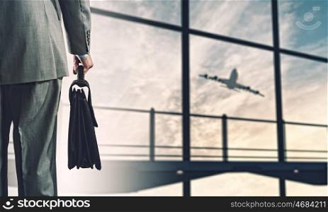 Business travel. Back view of businessman holding suitcase with airplane at background