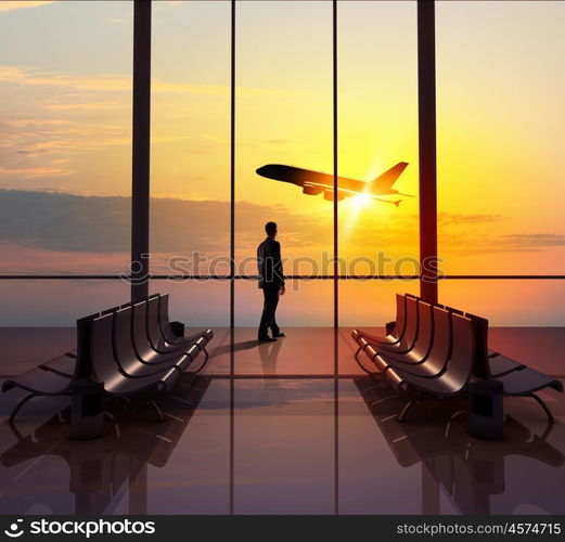 Business travel. Businessman at airport looking at airplane taking off