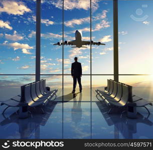 Business travel. Businessman at airport looking at airplane taking off