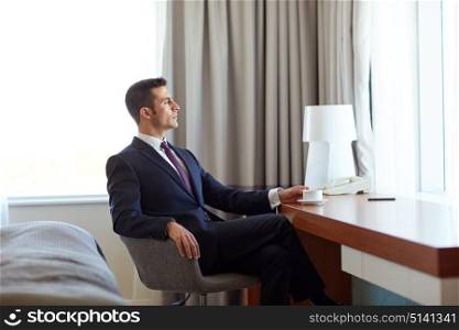 business trip and people concept - businessman drinking coffee at hotel room. businessman drinking coffee at hotel room