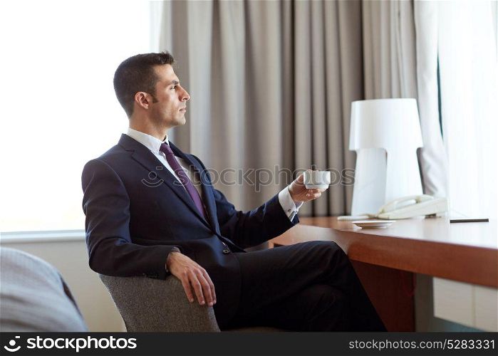business trip and people concept - businessman drinking coffee at hotel room. businessman drinking coffee at hotel room