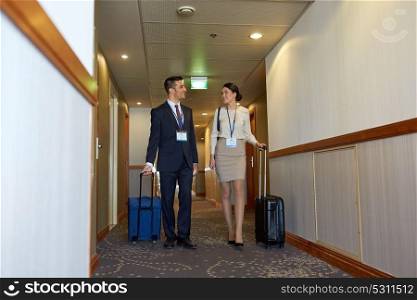 business trip and people concept - man and woman with travel bags and conference badges at hotel corridor. business team with travel bags at hotel corridor