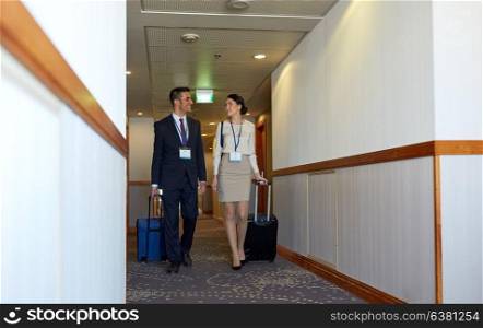 business trip and people concept - man and woman with travel bags and conference badges at hotel corridor. business team with travel bags at hotel corridor
