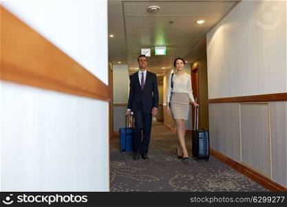 business trip and people concept - man and woman with travel bags at hotel corridor. business team with travel bags at hotel corridor