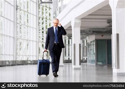 business trip, corporate and people concept - worried senior businessman walking with travel bag along office building or airport and thinking. worried senior businessman walking with travel bag