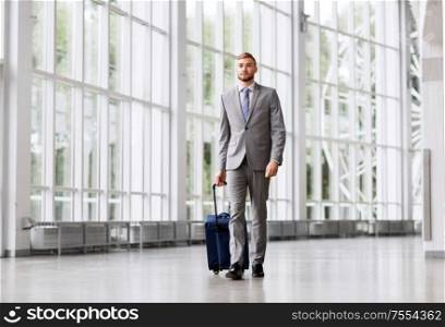 business trip, corporate and people concept - young businessman walking with travel bag along office building or airport. businessman with travel bag walking along office